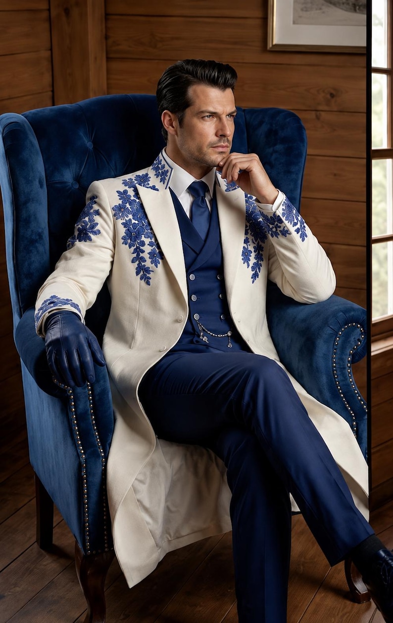 Puede incluir: Un abrigo largo de color crema con intrincados bordados florales azules en el cuello y los hombros, sobre un traje de tres piezas azul marino con corbata a juego, camisa blanca y guantes de cuero azul oscuro con cadena de bolsillo plateada.