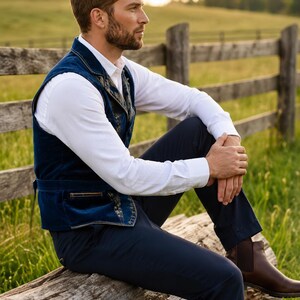 May include: A navy blue velvet vest featuring intricate gold embroidery along the lapels and pockets, worn over a crisp white long-sleeved button-down shirt, paired with dark navy trousers and brown leather ankle boots.