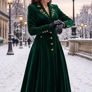 May include: A long-sleeved, floor-length dark green velvet coat featuring a high-low hemline, gold-toned buttons down the front, and intricate gold embroidery on the lapels. The coat is paired with black leather gloves and dark boots.
