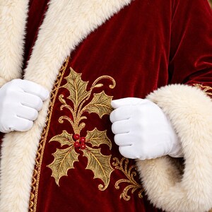 May include: A deep red velvet coat featuring a thick cream-coloured faux fur trim along the collar and cuffs. The front of the garment is decorated with intricate gold embroidery depicting holly leaves and small red berries along the lapel.