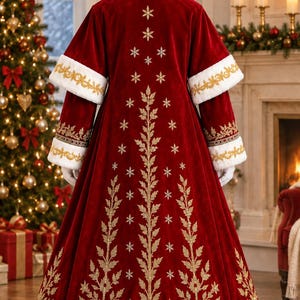 May include: A floor-length red velvet coat featuring white faux fur trim on the cuffs and hem. The back is decorated with gold embroidered leaf patterns and small star-like motifs arranged in a vertical, tree-like design.