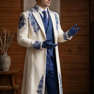 Puede incluir: Un abrigo largo de color crema con intrincados bordados florales azules en las solapas, los hombros y los pu&ntilde;os. El abrigo se lleva sobre un chaleco azul, una camisa blanca de cuello, una corbata azul y pantalones azules, junto con guantes de cuero azul.