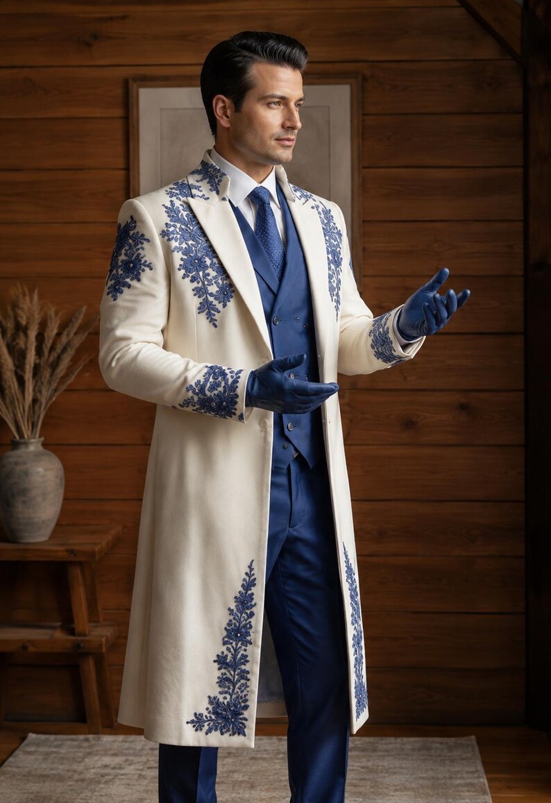 Puede incluir: Un abrigo largo de color crema con intrincados bordados florales azules en las solapas, los hombros y los pu&ntilde;os. El abrigo se lleva sobre un chaleco azul, una camisa blanca de cuello, una corbata azul y pantalones azules, junto con guantes de cuero azul.