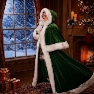 May include: A long, deep green velvet cloak featuring a thick, plush white faux fur trim along the hood, front opening, and hem. The garment is worn by a figure with a white beard and glasses, standing near a window with a snowy view.