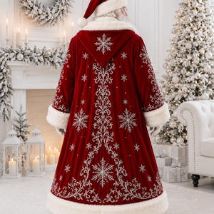 May include: A floor-length deep red velvet coat with a hood, featuring white faux fur trim on the cuffs, hem, and hood edge. The coat is decorated with intricate silver embroidery in swirling patterns and snowflake motifs throughout.