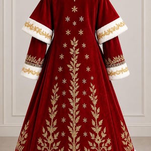May include: A floor-length deep red velvet coat featuring a white faux fur collar and hem. The sleeves have white faux fur cuffs with gold embroidery. The back is decorated with vertical gold embroidered branches and small star-shaped motifs.