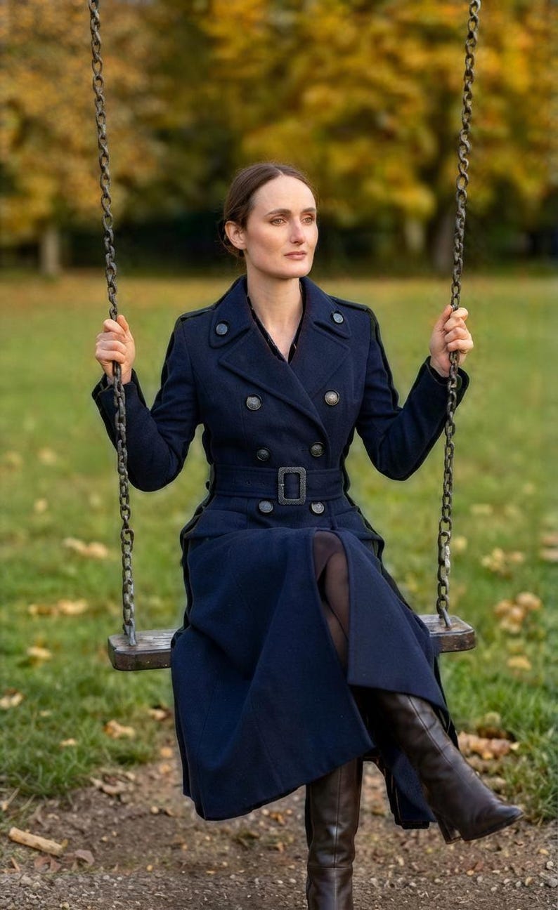 May include: A long, double-breasted navy blue wool coat featuring a structured collar, dark metallic buttons, and a matching belt with a rectangular buckle. The coat has long sleeves and a tailored fit, extending down to the lower legs.