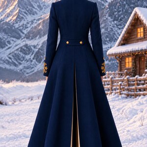 May include: A floor-length navy blue coat featuring a high collar, long sleeves with gold embroidery at the cuffs, and a back vent revealing a beige lining. The waist is accented with a horizontal tab featuring two gold buttons, and black boots.