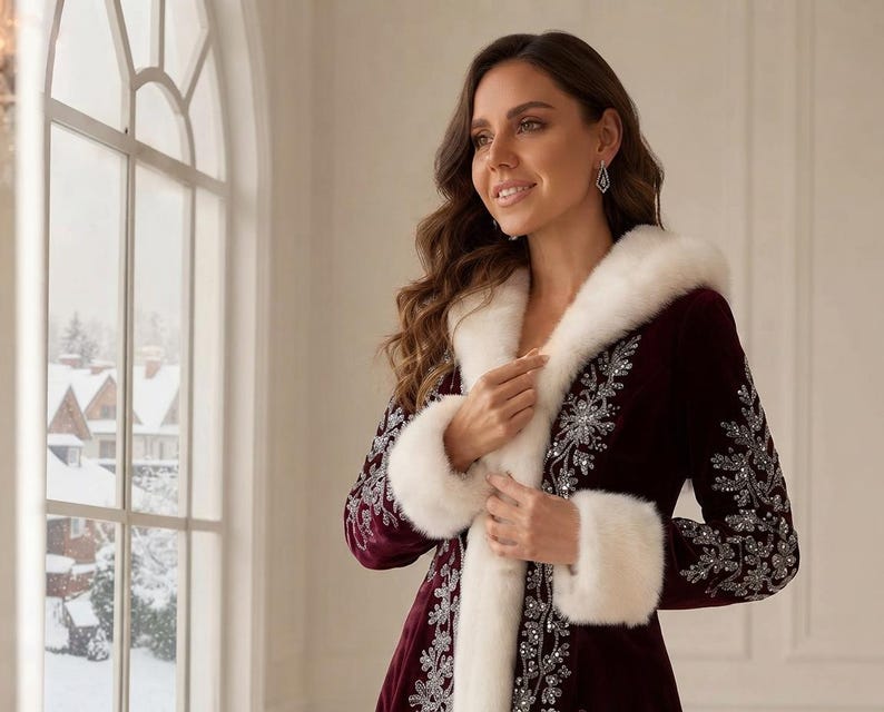 May include: A deep burgundy velvet coat featuring a white faux fur hood and cuffs. The coat is adorned with intricate silver embroidery and sequin detailing along the front opening and sleeves, creating a decorative pattern against the dark fabric.