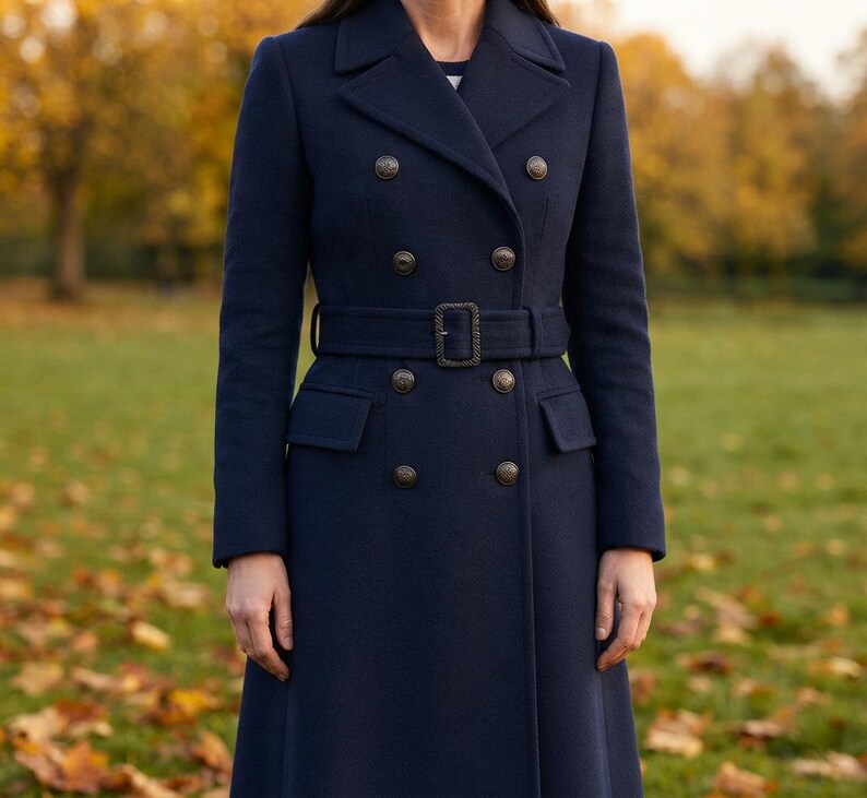 May include: A navy blue double-breasted coat featuring a structured collar, long sleeves, and a matching fabric belt with a rectangular buckle. The coat is adorned with two vertical rows of metallic buttons and includes two flap pockets at the waist.
