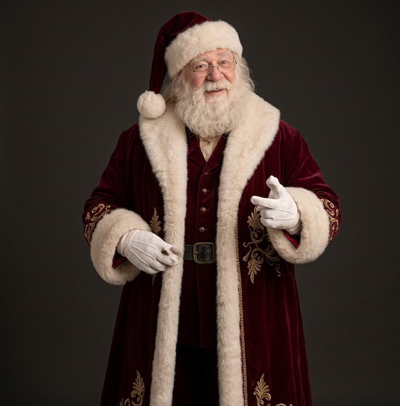May include: A Santa Claus figure wearing a deep burgundy velvet coat and matching hat, both trimmed with thick white faux fur. The coat features gold embroidery along the cuffs and hem, a dark belt with a buckle, and white gloves.