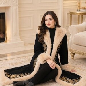 Pu&ograve; includere: Un cappotto nero a maniche lunghe con ampio colletto e polsini in pelliccia sintetica beige, decorato con intricati ricami floreali dorati lungo i bordi anteriori e l'orlo, abbinato a leggings neri e stivaletti neri.