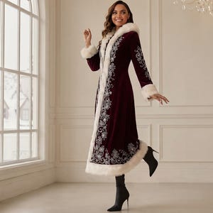 May include: A long, deep burgundy velvet coat featuring a white faux fur trim along the hood, front opening, cuffs, and hem. The coat is decorated with intricate silver floral embroidery patterns running down the front and along the sleeves.