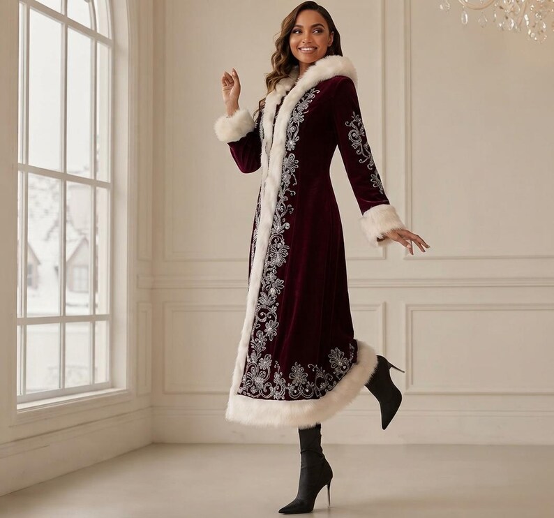 May include: A long, deep burgundy velvet coat featuring a white faux fur trim along the hood, front opening, cuffs, and hem. The coat is decorated with intricate silver floral embroidery patterns running down the front and along the sleeves.