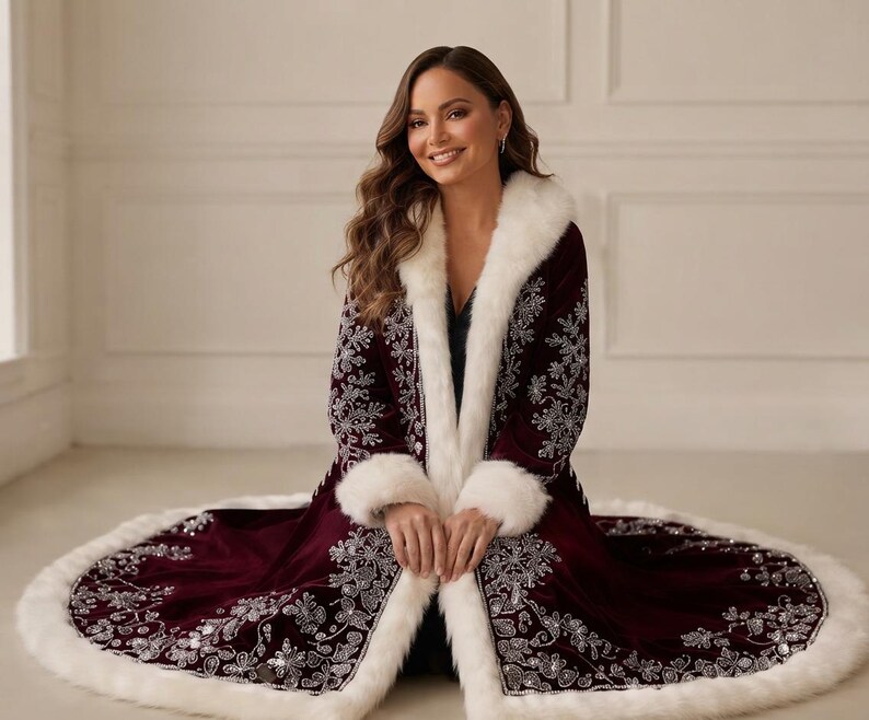 May include: A deep burgundy velvet coat featuring a white faux fur trim along the collar, cuffs, and hem. The coat is decorated with intricate silver embroidery in floral and snowflake patterns across the front panels and the lower skirt area.
