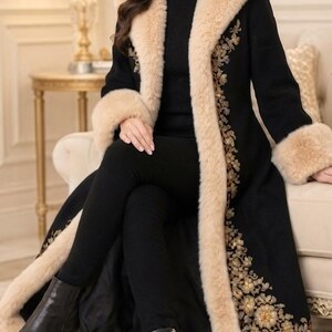 Pu&ograve; includere: Un lungo cappotto nero caratterizzato da un folto bordo in pelliccia sintetica beige lungo il colletto, l'apertura frontale e i polsini. Il cappotto &egrave; decorato con intricati ricami floreali color oro e bronzo sui pannelli anteriori.