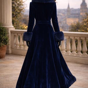 May include: A floor-length navy blue velvet coat featuring a wide faux fur collar, matching faux fur cuffs, and a faux fur trim along the bottom hem. The coat includes a fitted waist with a belt, long sleeves, and a flared skirt silhouette.
