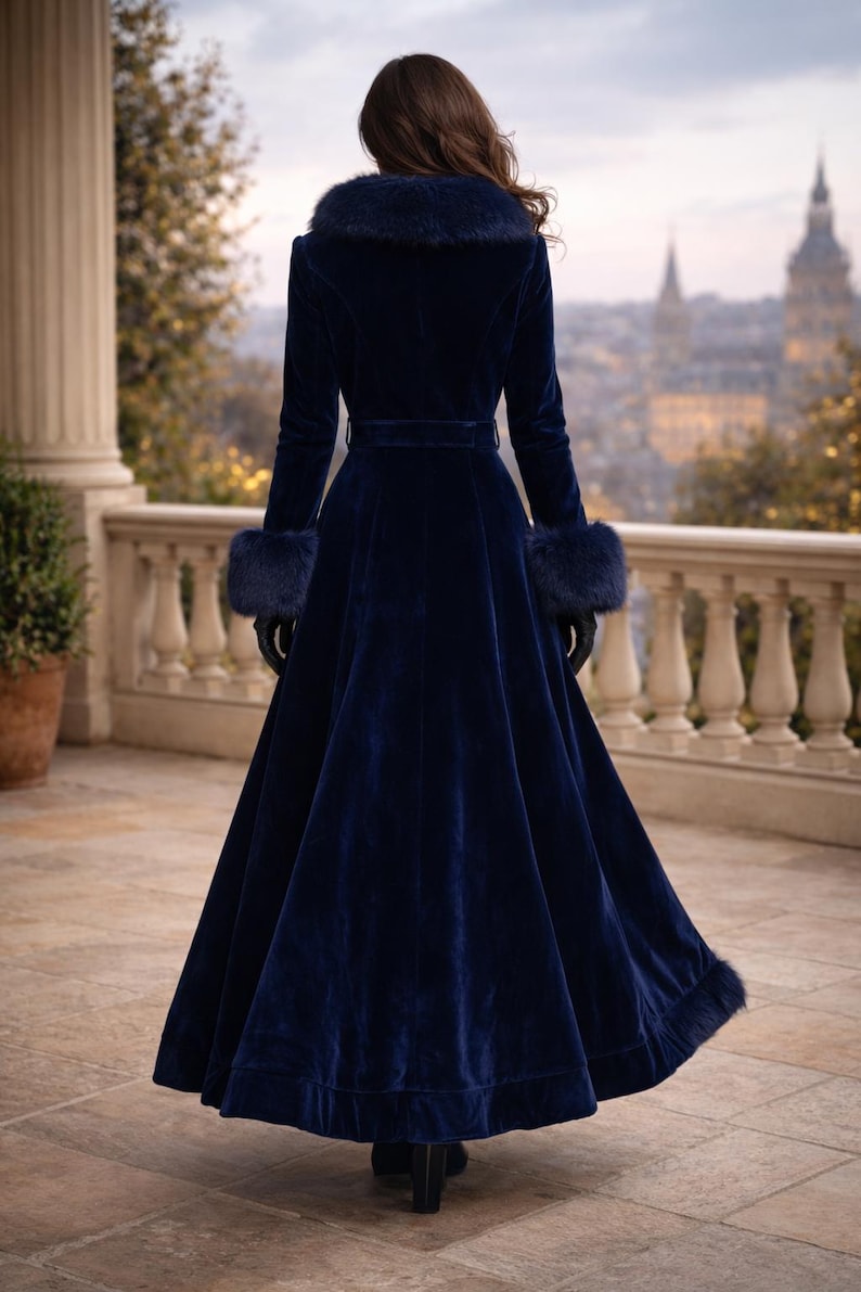 May include: A floor-length navy blue velvet coat featuring a wide faux fur collar, matching faux fur cuffs, and a faux fur trim along the bottom hem. The coat includes a fitted waist with a belt, long sleeves, and a flared skirt silhouette.