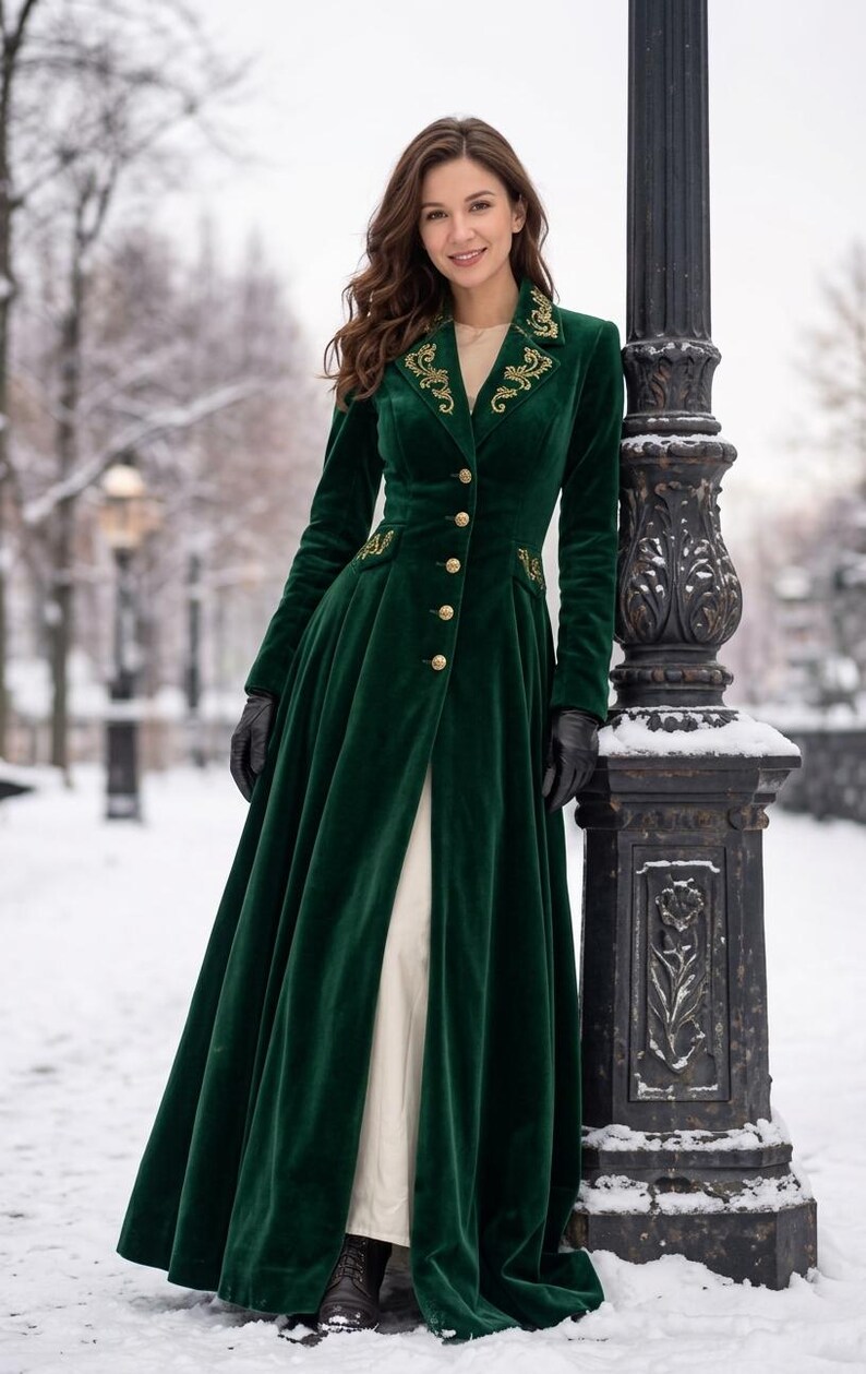 May include: A floor-length dark green velvet coat featuring gold embroidery on the lapels and waist pockets, a row of gold buttons down the front, long sleeves, and a flared skirt silhouette worn over a light-coloured garment.