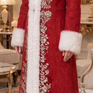 May include: A long red coat featuring white faux fur trim along the collar, cuffs, and hem. The coat is decorated with intricate silver floral embroidery running vertically along the front panels. It is paired with black pointed-toe ankle boots.