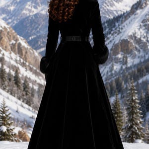 May include: A floor-length black velvet coat featuring a high collar with fur trim, long sleeves with fur-trimmed cuffs, and a matching black belt cinched at the waist. The coat has a flared skirt silhouette and is worn with black heeled boots.