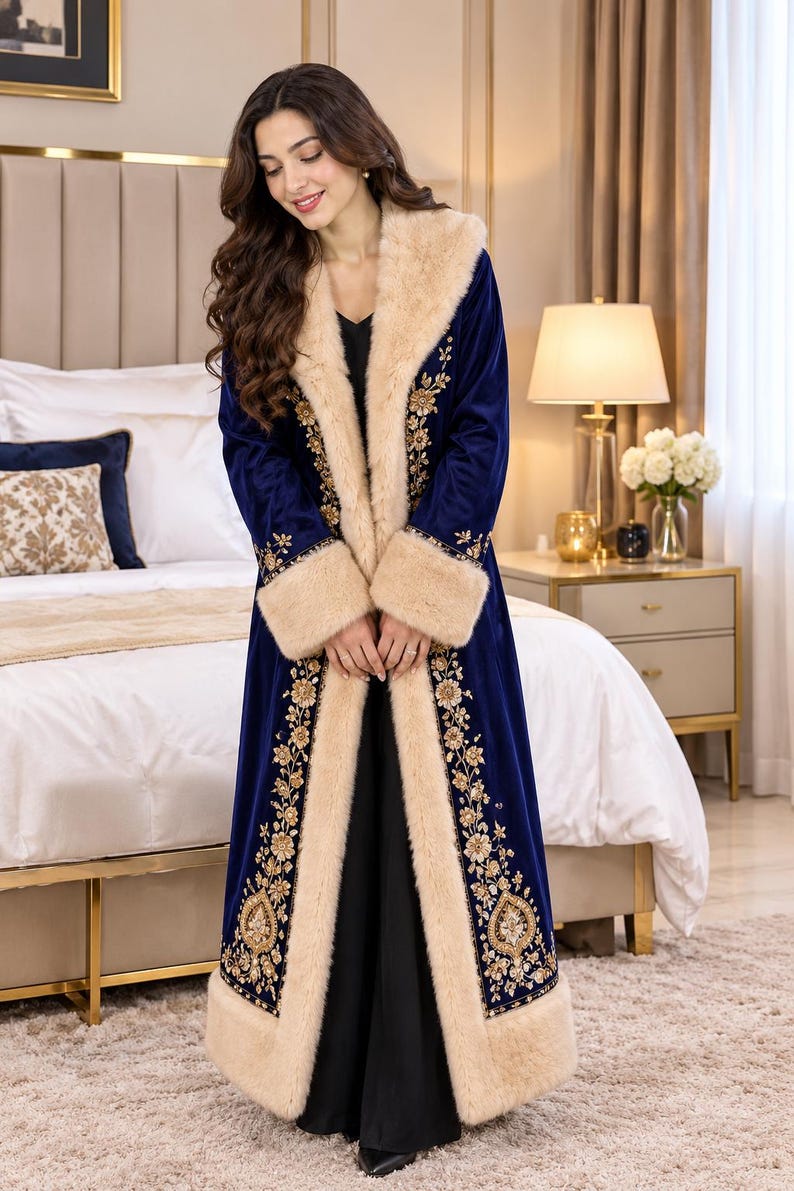 May include: A long, deep blue velvet coat featuring a thick, beige faux fur trim along the collar, front opening, and sleeve cuffs. The coat is decorated with intricate gold floral embroidery patterns running vertically along the front panels.