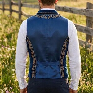 May include: A deep blue vest featuring intricate gold embroidery along the neckline and side panels. The garment is worn over a white long-sleeved shirt and paired with dark trousers, showcasing a structured fit with a buttoned back adjustment strap.