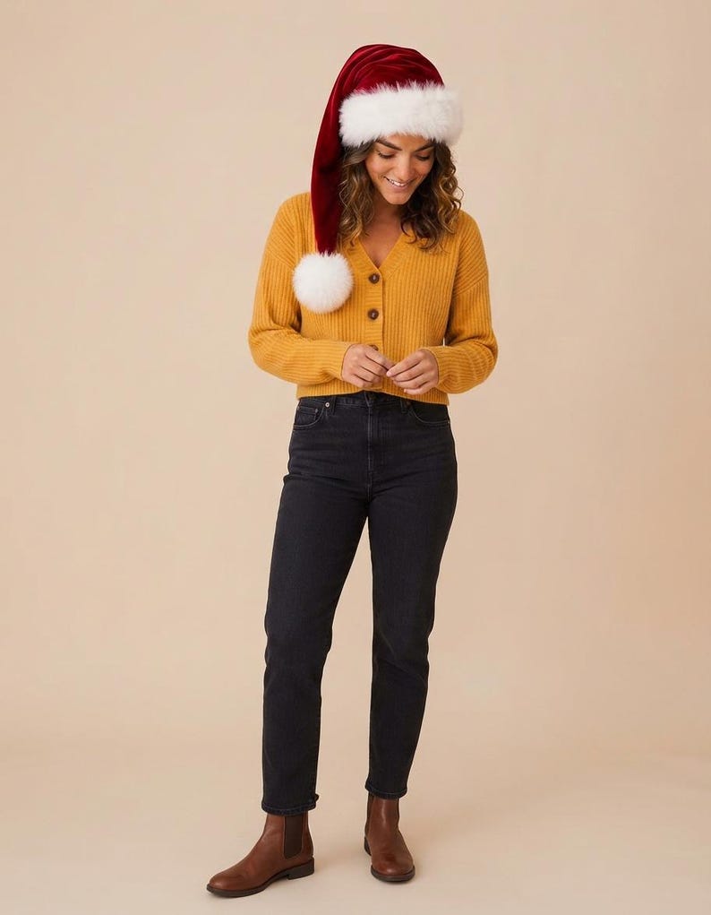 May include: A mustard yellow ribbed V-neck cardigan with buttons, paired with black denim jeans and brown leather ankle boots. A long red velvet Santa hat with a white faux fur trim and a large white pom-pom rests on the head.
