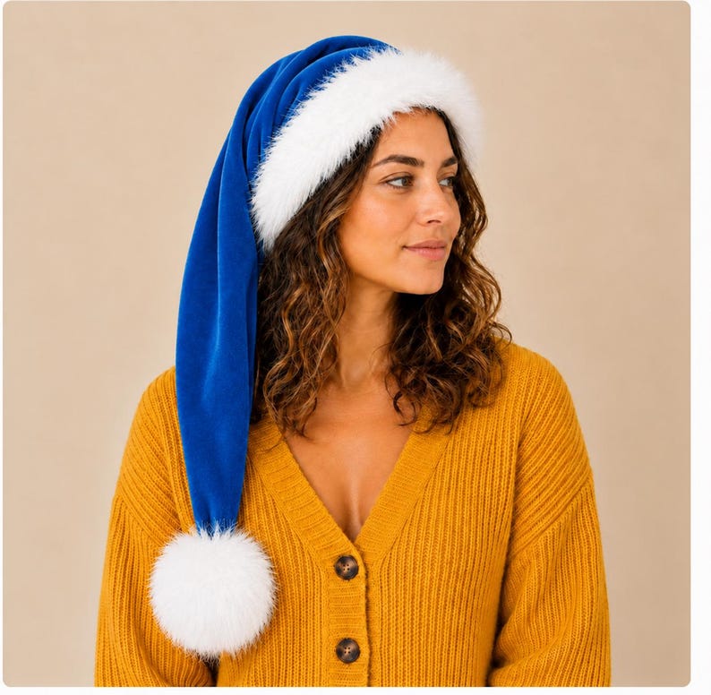 May include: A long, royal blue velvet hat featuring a thick, white faux fur trim around the base and a large, fluffy white pom-pom at the pointed end. The hat is designed with a soft, plush texture and a deep, vibrant blue color.
