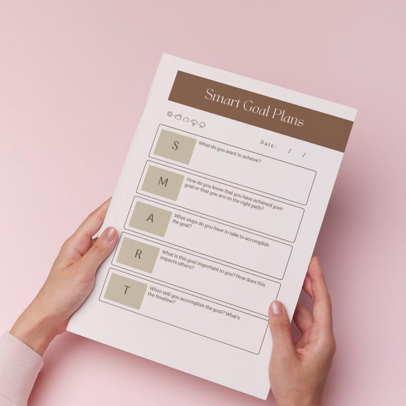 A person's hands are holding a sheet of paper titled "Smart Goal Plans" against a pink background.