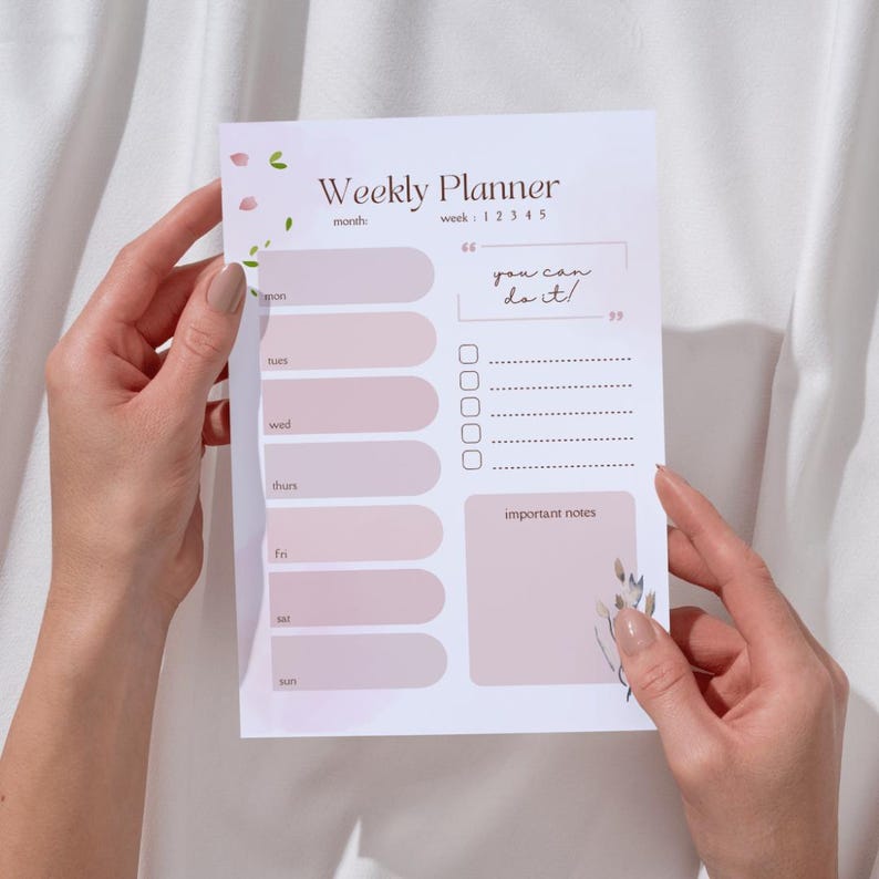 A person's hands holding a white paper with a weekly planner design.