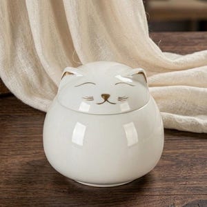 Peut inclure: Un bocal en verre transparent avec un couvercle argenté. Le bocal est rempli d'une substance de couleur claire, peut-être un aliment. Le bocal est posé sur une surface blanche.