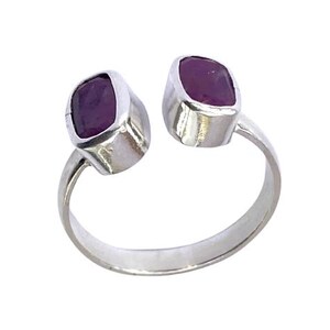 May include: A silver-toned ring featuring two bezel-set, deep purple gemstones. The ring's design is open, with the gemstones positioned on either side of the finger. The gemstones have a slightly irregular, organic shape.