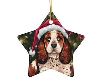 Puede incluir: Adorno navideño en forma de estrella con un Basset Hound con un gorro de Papá Noel. El perro tiene pelaje marrón y blanco, orejas largas y una expresión triste. El adorno tiene una cuerda dorada para colgar.