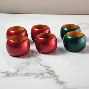 May include: A set of six round napkin rings with a smooth, glossy finish. Four of the rings are a vibrant red color, and two of the rings are a deep forest green color. Each ring features a natural, light-colored wood interior finish.