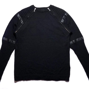 Puede incluir: Jersey negro de punto con detalles de cuero en hombros y mangas. Cuenta con dos cremalleras plateadas cerca de los hombros. Una prenda de manga larga.