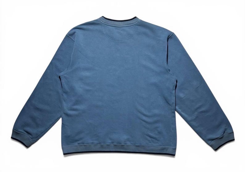 May include: A light blue sweatshirt with long sleeves, a crew neck, and a dark blue trim. The garment is made of a soft material and is laid flat on a white surface. The sweatshirt has a simple, classic design.