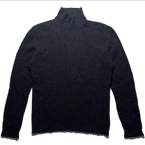 May include: A dark grey turtleneck jumper with long sleeves. The jumper has a ribbed texture and a high, folded collar. The garment is made of a soft, possibly knitted material, and is suitable for cooler weather. The jumper is displayed on a white background.