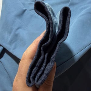 May include: A light blue sweatshirt with a small black Nike logo. The cuff of the sleeve is dark blue and folded over. The sweatshirt is made of a soft material.