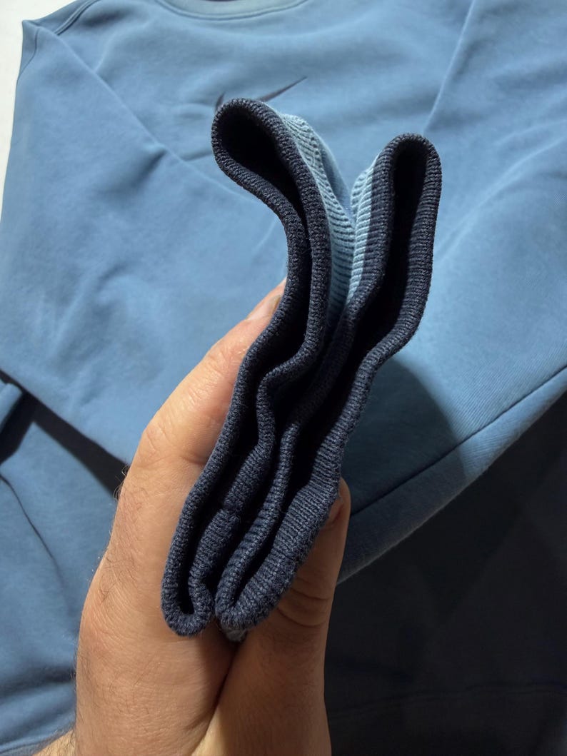 May include: A light blue sweatshirt with a small black Nike logo. The cuff of the sleeve is dark blue and folded over. The sweatshirt is made of a soft material.