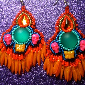 May include: A pair of colorful beaded earrings with a turquoise green stone, orange fringe, and pink skull accents.