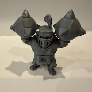 May include: A gray 3D-printed figurine of a knight, holding two large spiked maces. The knight is wearing a helmet with a plume and armor. The figurine is standing on a white surface.