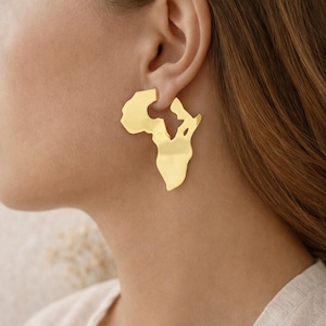 Peut inclure: Boucles d'oreilles dorées en forme de continent africain. Les boucles d'oreilles sont de couleur or unie et brillante et se portent à l'oreille. Les boucles d'oreilles sont d'un design simple mais élégant.