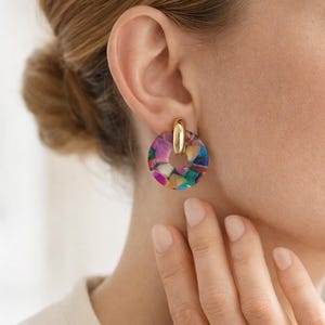 Op de afbeelding: Goudkleurige oorringen met een kleurrijk, mozaïekachtig ontwerp. De oorbellen hebben een cirkelvorm met een goudkleurige pin. Het mozaïekontwerp bevat verschillende kleuren, waaronder roze, blauw, groen en geel.