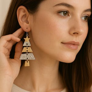 Puede incluir: Pendientes de árbol de Navidad en tonos plateado y dorado. Los pendientes presentan una estrella en la parte superior, seguida de formas geométricas en capas. Fabricados en metales mixtos, tienen un diseño festivo. Un accesorio navideño único.