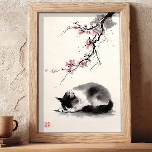 May include: A framed watercolour painting depicting a sleeping cat under a flowering branch. The cat is black and white, and the flowers are pink. The artwork is in a wooden frame and sits on a wooden shelf.