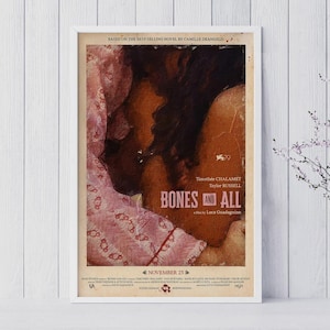 Puede incluir: Un póster de película enmarcado de "Bones and All" con Timothée Chalamet y Taylor Russell. El póster tiene una paleta de colores cálidos con el título en letras en negrita. La fecha de lanzamiento, 23 de noviembre, también es visible.