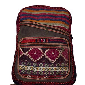 May include: A brown backpack with a colourful woven design. The backpack features a front pocket with a geometric pattern in shades of pink, purple, and white. The top section has horizontal stripes in red, orange, blue, and green.