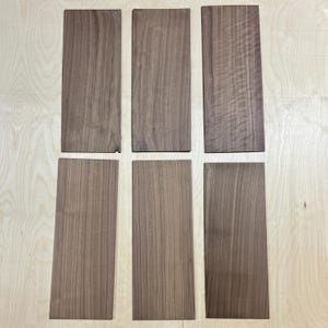May include: Six rectangular pieces of unfinished wood with a natural brown color and visible wood grain. The pieces are arranged in two rows of three on a light-colored wooden surface.