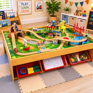 May include: A wooden train table featuring a multi-level track system with a mountain tunnel, a red bridge, and various buildings. The table surface displays a printed landscape, and three red storage bins underneath contain assorted toy accessories.